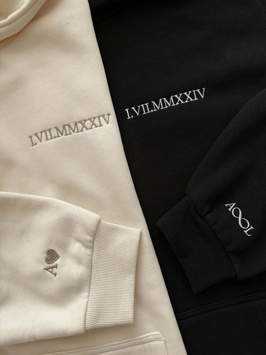 Detailaufnahme der hochwertigen Stickerei: Wunschdatum in römischen Ziffern auf einem flauschigen Hoodie