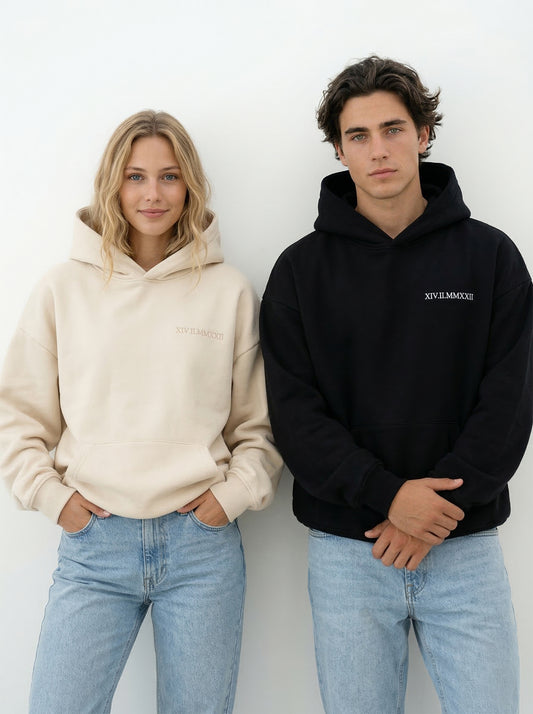 Paar trägt schwarze personalisierte Partner Hoodies mit besticktem Datum in römischen Ziffern im Oversized Fit